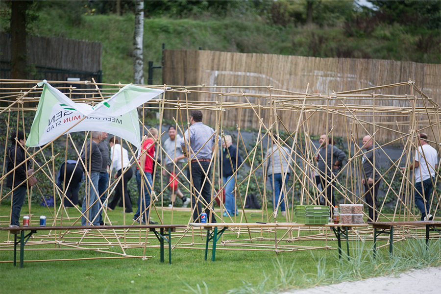 Een groep mensen die een huis bouwen van bamboestokken als teambuildingsactiviteit in Panheel, Limburg.