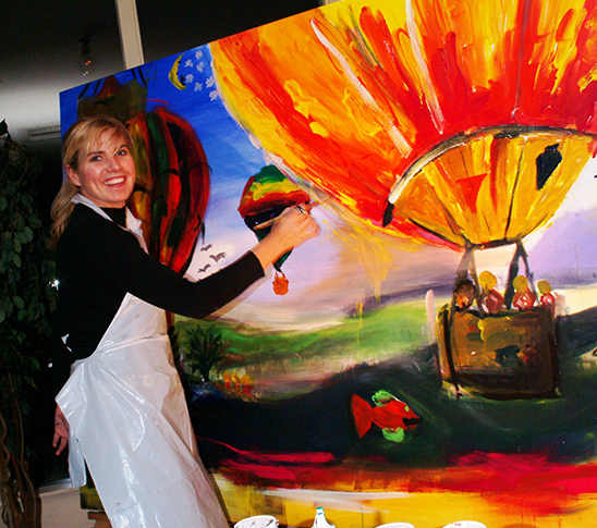 Vrouw staat trots bij een schilderij terwijl ze aan het verven is.