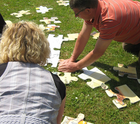 Volwassenen die een reuze puzzel aan het maken zijn tijdens een personeelsuitje of bedrijfsuitje in Midden-Limburg.