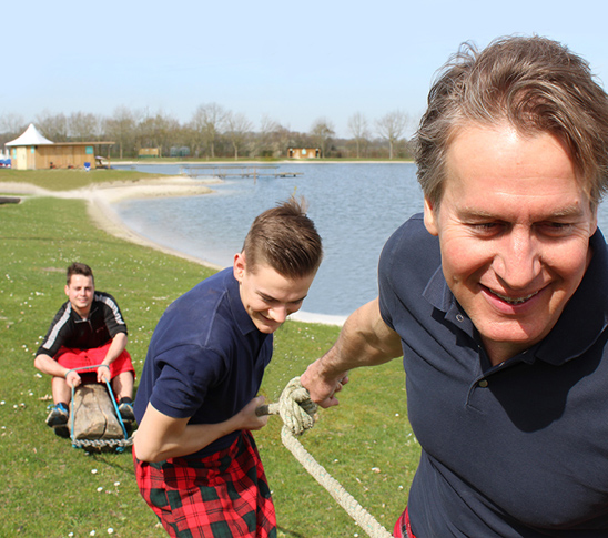 Twee mannen trekken een boomstam met daarop hun teamgenoot vooruit als teambuildingsactiviteit.